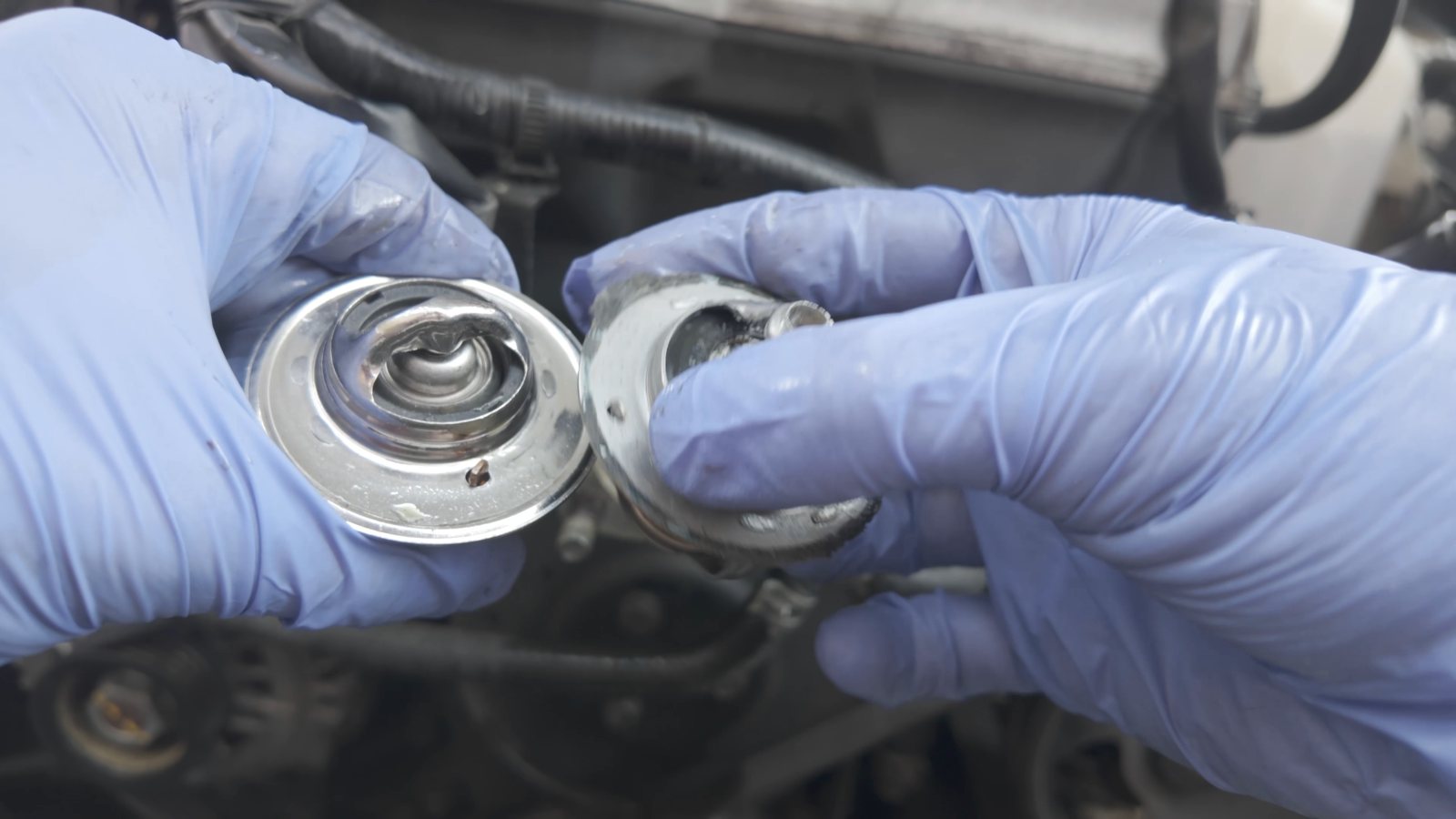 Gloved hands holding an engine thermostat and housing