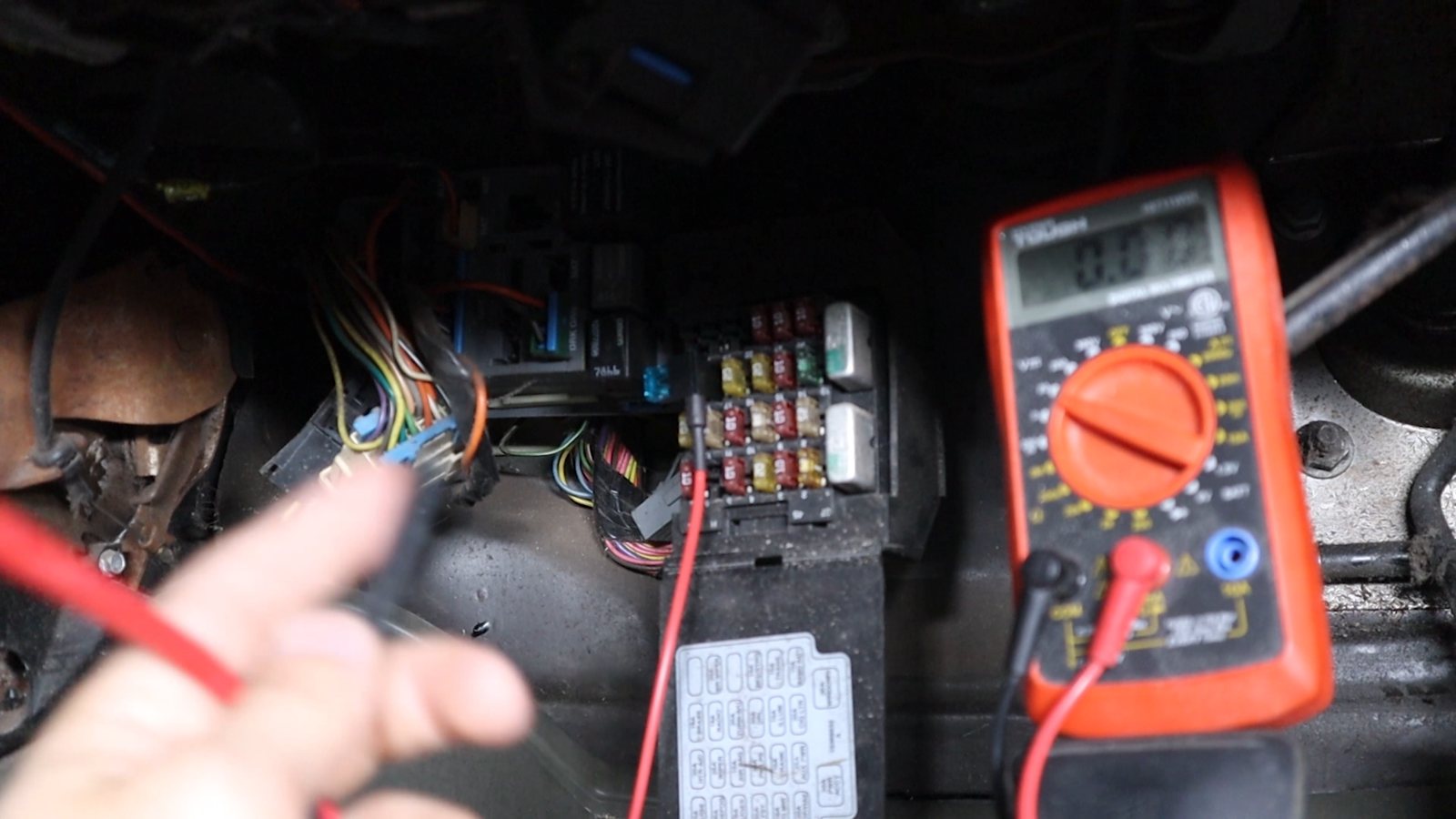Multimeter and test leads being used near a vehicle fuse panel