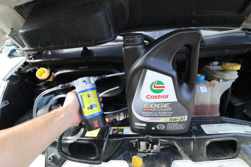 Chris holding a 12V oil extractor pump beside an oil jug in his van engine bay